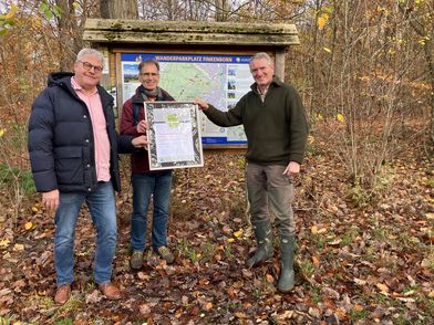 Frank Lücke von Hameln Marketing und Tourismus, Hans-Georg Sievers vom Naturpark Weserbergland und Carsten Bölts vom Hamelner Forstamt stehen mit der Urkunde im Wald