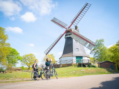 Zwei Radfahrer stehen mit ihren Rädern vor einer Mühle und gucken sie sich an