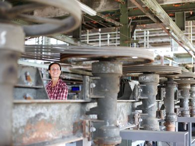 Junge Frau steht in der Maschinenhalle zwischen Eisenkonstruktionen.