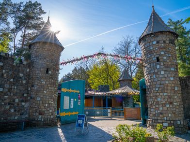 Zwei Steintürme rahmen das türkise Eingangstor des Magic Parks in Verden unter blauem Himmel ein.