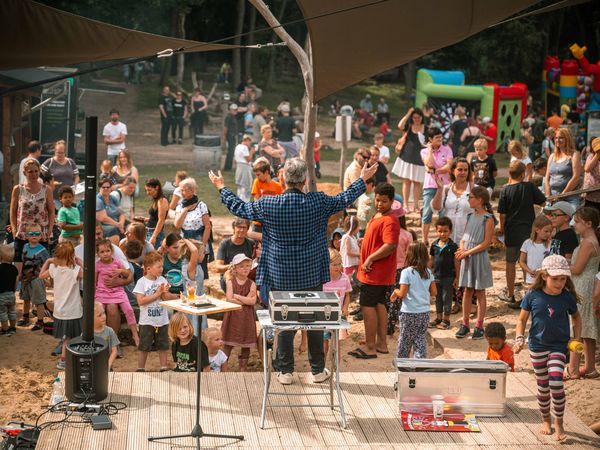 Ein Zauberkünstler auf einer kleinen Bühne, davor ein Publikum mit vielen Kindern.