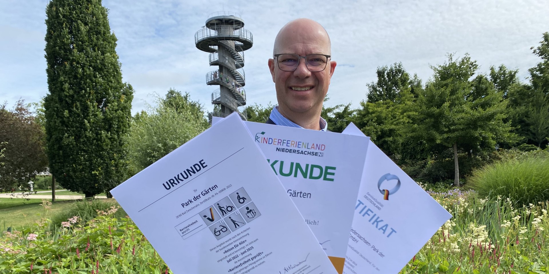 Christian Wandscher mit den drei touristischen Zertifikaten „Besonders kinderfreundlich“, „Barrierefreiheit geprüft“ und „ServiceQualität Deutschland“, © Gartenkulturzentrum Niedersachsen - Park der Gärten gGmbH